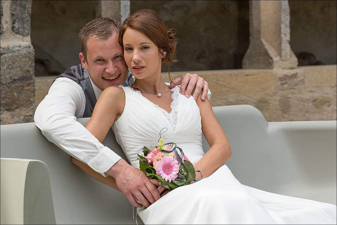 La mariée est assise sur un banc et le marié est accroupi derrière elle