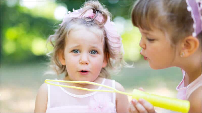 Deux soeurs jouent à faire des bulles de savon, la plus jeune souffle en regardant le photographe