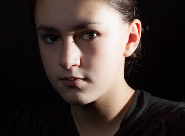 Une jeune fille habillée en noir regarde fixement l'objectif lors d'une séance de photo studio