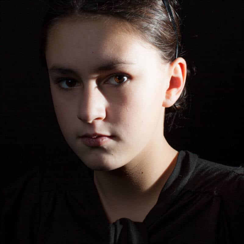 Une jeune fille habillée en noir regarde fixement l'objectif lors d'une séance de photo studio