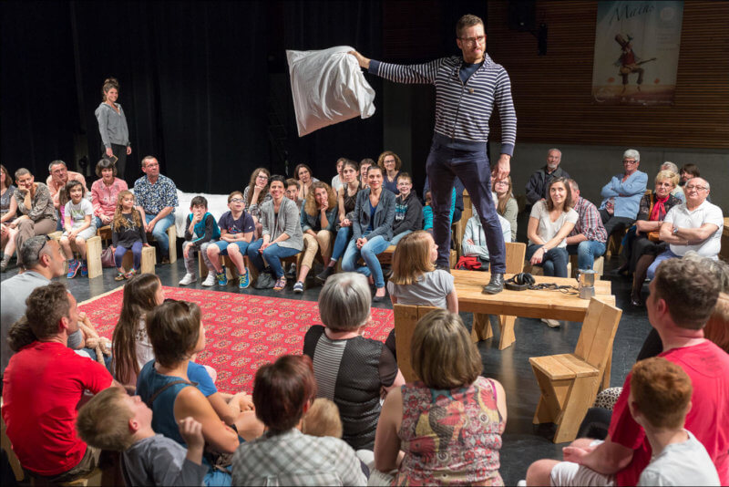 Un homme qui interprète un spectacle, se tient debout sur une table avec un oreiller dans la main