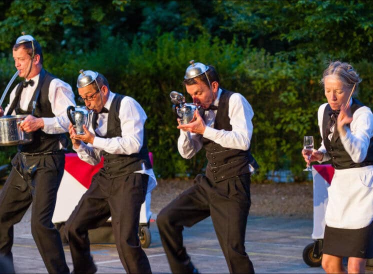 Quatres comédiens déguisés en serveurs de café jouent de la musique avec des ustensiles de cuisine