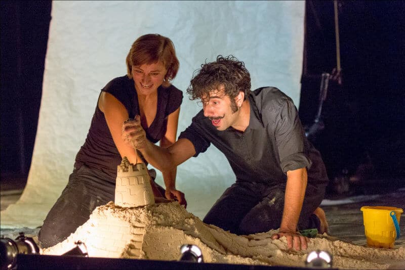 Deux artistes construisent un chateau de sable. L'homme laisse couler le sable qu'il a dans sa main.