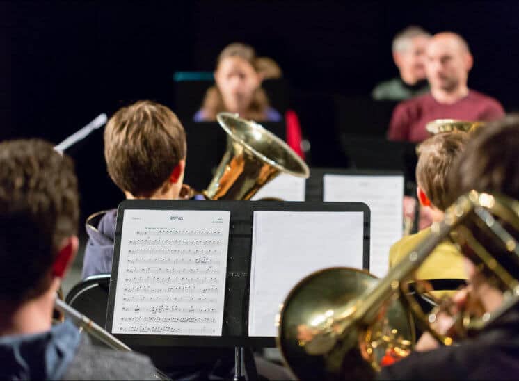 Lors d'un concert d'une école de musique, les jeunes élèves sont de dos avec leurs instruments. La partition est sur le pupitre