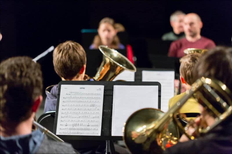 Lors d'un concert d'une école de musique, les jeunes élèves sont de dos avec leurs instruments. La partition est sur le pupitre