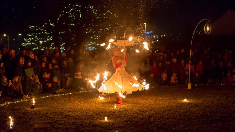 L'artiste de ce spectacle se déplace avec une robe et un parapluie sur lesquels sont fixés des petites flammes. Le public est rassemblé autour de la scéne