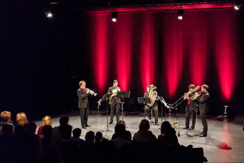 Un groupe de cinq musiciens se produit sur une scéne éclairée de lumière rouge