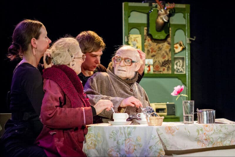 Un spectacle de marionnette à taille humaine où les deux personnes prennent le thé devant une table