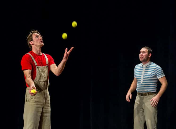 Un artiste jongle avec cinq balles alors que l'autre le reagarde