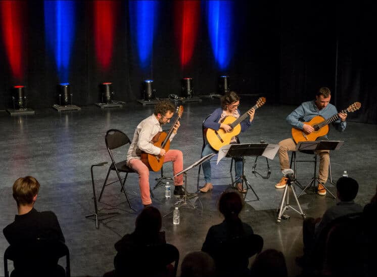 Les trois musiciens du Trio Explora jouent de la guitare sur la scène de la salle LES JUSTES