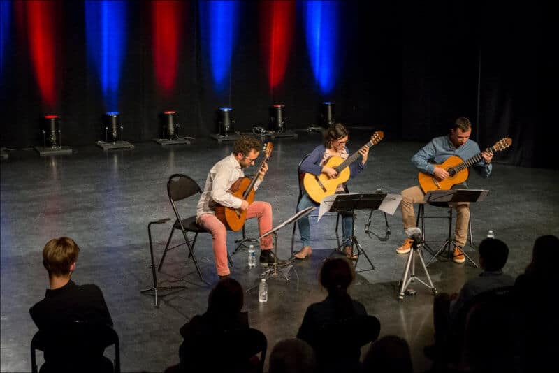 Les trois musiciens du Trio Explora jouent de la guitare sur la scène de la salle LES JUSTES