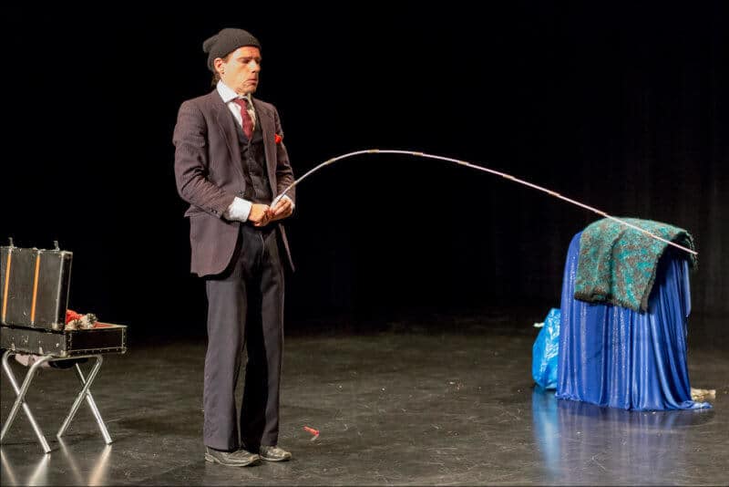 L'ariste de ce spectacle, vêtu d'un costume et d'un bonnet, tient un mètre pliant devant lui pour représenter qu'il urine