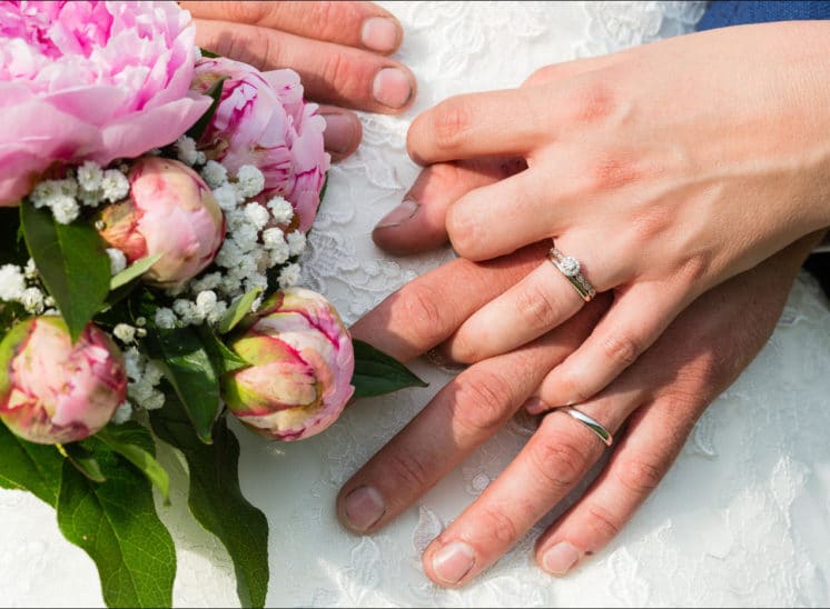 Gros plan des mains des mariés avec le bouquet