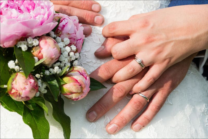 Gros plan des mains des mariés avec le bouquet