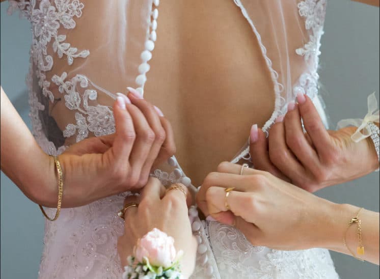 Les fille d'honneur boutonnent la robe de la mariée